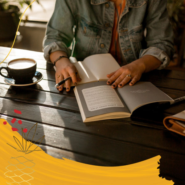 Person sitting in a coffee shop with a coffee and a journal